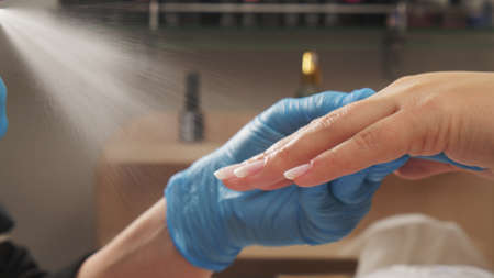 Manicurist sprays antiseptic on the nails before treating old  acrylic nails. Treatment of nails with a disinfectant before manicure. Applying a disinfectant to women's hands.の写真素材
