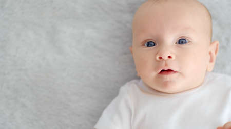 Child's face of a Happy newborn baby looking to camera. Healthy newborn baby in a white t-shirt with...