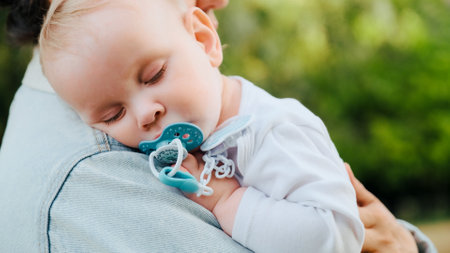 Baby sleeps on his mother's shoulder, in the park. Close-up of a sleeping little child on mom,...
