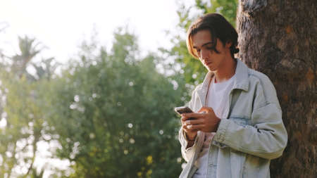 Sad man with a mobile phone in the park. Young guy received an sms with bad news. Young man in the park picks up his cell phone and looks at the screen.の写真素材