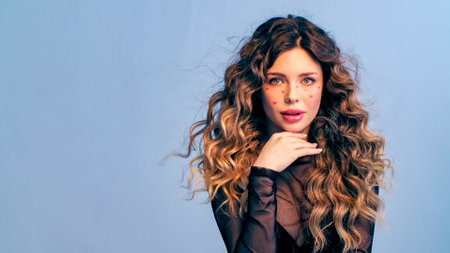 Beautiful model with drawn hearts on her cheeks posing in the studio. Fashion model is photographed in a photo studio looking at camera. Beautiful young woman with long hair.の写真素材