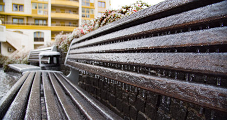 Frozen city bench in the ice icicles. Climatic icing.   Icy city bench after winter natural disaster. City environment in a winter.の写真素材