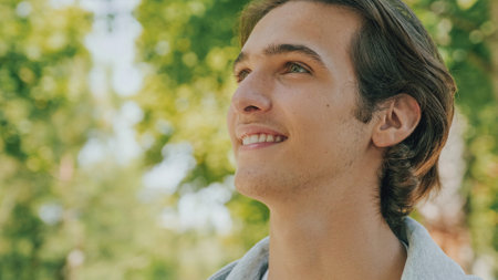 Closeup portrait of happy handsome young man at the park in summer. Cheerful teenager looks to the...