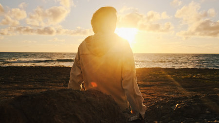 Man on a beach is looking distance during beautiful summer sunset. Human looks to the sun over horizon in the morning while sunrise. Happy person contemplates the beauty of nature. Freedom concept.の写真素材
