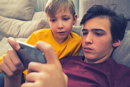 Boys spending time in a social network using mobile phones.  Children with smartphones at home. White kids using cell phones for gaming. People and social media conceptの写真素材