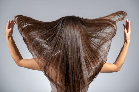 Back view of a brunette woman with a long straight hair. Young   model with  beautiful hair - isolated on white background. Young girl with hair flying in the wind.の写真素材