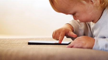 Small Baby pressing and scrolling with finger on phone touch screen. Cute Little child learns to use new internet technologies. Baby playing with cellphone, at home in the evening.の写真素材