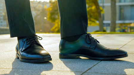 Close-up view to the businessman in a black new classic  shoes outdoors. Legs of  businessman in fashionable glossy  shoes on the sidewalk. Business concept. Stylish men wears. Low angle.の写真素材