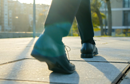 Legs of a businessman in fashionable shoes walking outdoors. Business concept. Close-up view to the businessman in a black new shoes walks on the street. Stylish men wears. Low angle. Rear view.の写真素材