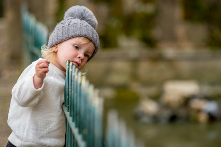 Cute blonde kid in a gray hat exploring the world around him in a park. Adorable caucasian child...