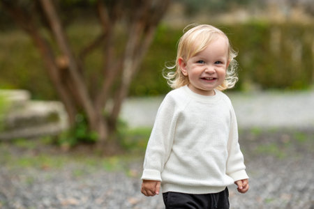 Cute blonde kid smiling outside in a park. Happy kid playing outside on a spring day. Adorable caucasian child walking in a garden, looking and smiling at the camera.の写真素材
