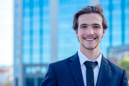 Smiling confident businessman near a business center. A young businessman in a suit outside a tradecenter. A young businessman near a modern tall glass building.の写真素材
