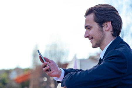 Smiling businessman near a business center with a cell phone. A happy young businessman looking at a...
