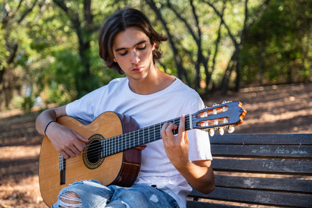 Guitarist plays on guitar outdoors.  Handsome guy plays the guitar on the nature sitting on a bench....