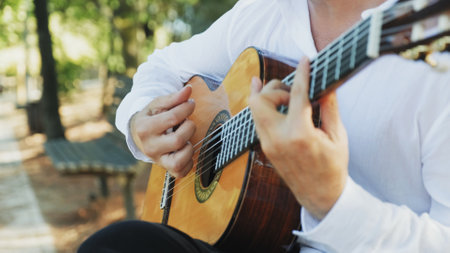 Guitarist plays on the guitar. Professional guitarist plays guitar outdoors. Musician plays a classical guitar in the park. A man in a white shirt plays a musical instrument outside the house.の写真素材