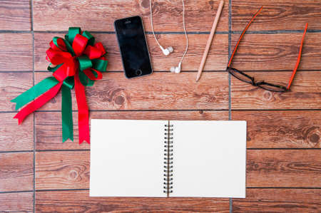 Wood texture mock up with notebook, ribbon, smart phone, earphone, pencil and glasses. View from above. Christmas Day.の写真素材