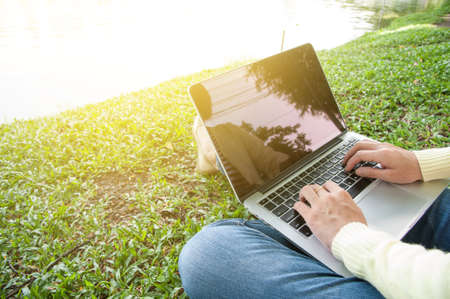 Woman sit to use silver laptop at parks and building in the city with gold light, Bangkok Thailandの写真素材