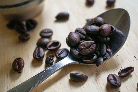Close of dark roasted coffee bean and spoon on wooden board