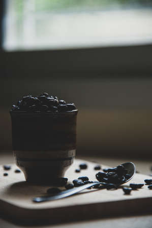 Silhouette roasted coffee bean in antique cup and teaspoon on wooden backdrop with low light, on right of frameの写真素材