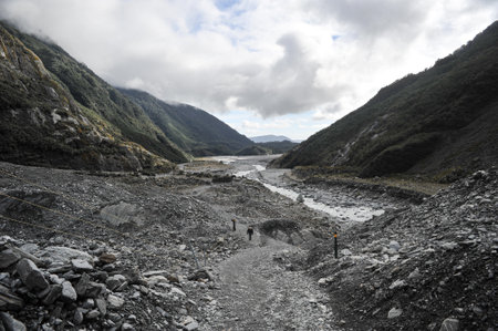 top view of stream of glacier with little tourists among stone and cloudy sky in autumnの写真素材