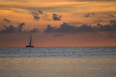 Sailboat heading towards the horizon under clouds and calm sea