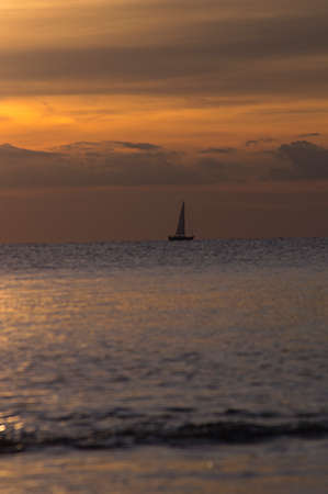 Lonely sailboat against light in the calm sea accompanied by clouds