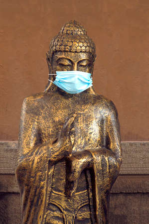 Buddha figure with surgical mask on a background of a handmade wall