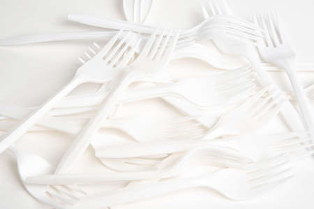 An array of unused, non-biodegradable white plastic fork set on a white background.