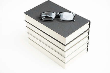 A neatly stacked set of five monochromatic cloth-bound books with reading eyeglasses on a plain white background.の写真素材