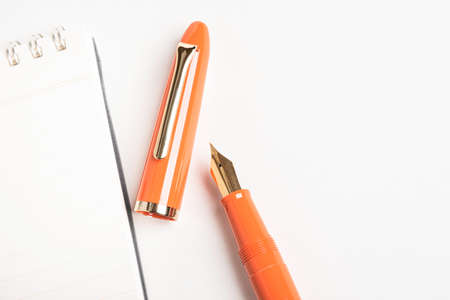 A shiny orange fountain pen together with a spiral-bound ruled notebook.の写真素材