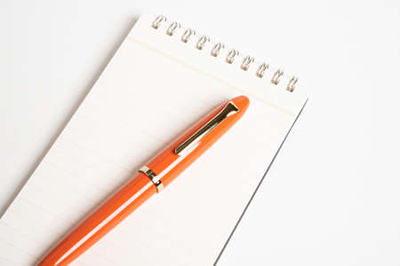 A shiny orange fountain pen together with a spiral-bound ruled notebook.の写真素材
