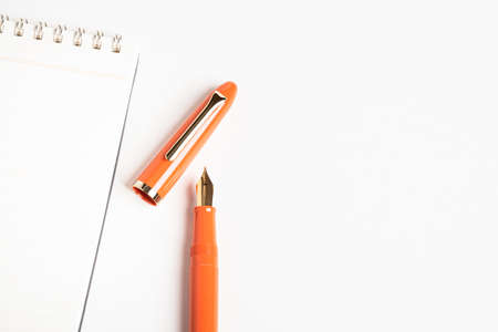 A shiny orange fountain pen together with a spiral-bound ruled notebook.の写真素材