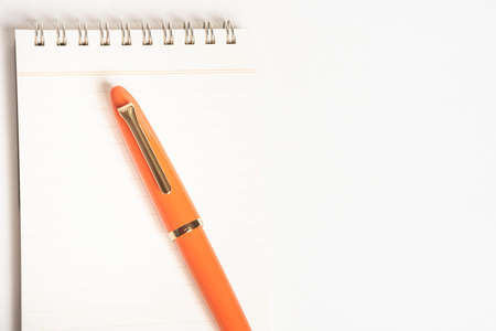 A shiny orange fountain pen together with a spiral-bound ruled notebook.の写真素材