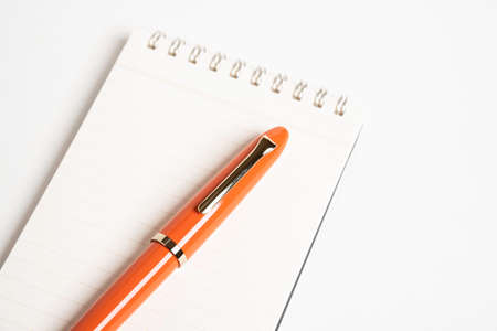 A shiny orange fountain pen together with a spiral-bound ruled notebook.の写真素材