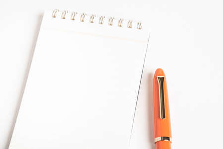A shiny orange fountain pen together with a spiral-bound ruled notebook.の写真素材
