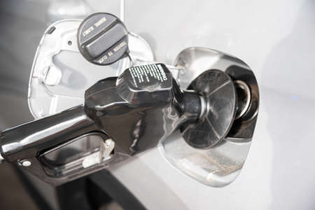 A silver-color vehicleâs empty gas tank is being filled with fuel at the gas station.の写真素材