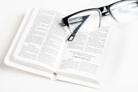 An open white portable pocket bible with a pair of clear reading glasses set on plain white background.の写真素材