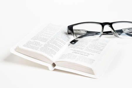 An open white portable pocket bible with a pair of clear reading glasses set on plain white background.の写真素材