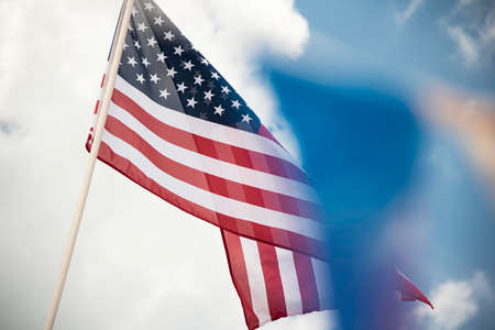 An American flag set on bright blue sky with white clouds accented by colored ribbon banner.