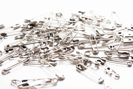 A macro shot of a bunch of metal safety pins scattered on a plain white background.の写真素材