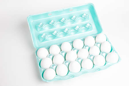 A close-up shot of a bright green polystyrene crate full of white eggs set on a white background.