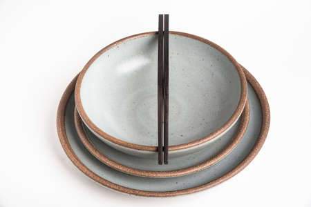 A pair of oriental black wooden chopsticks resting on a dinner service of textured stoneware plates...