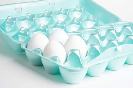 A close-up shot of a polystyrene egg crate with four white eggs set on a plain neutral background.の写真素材