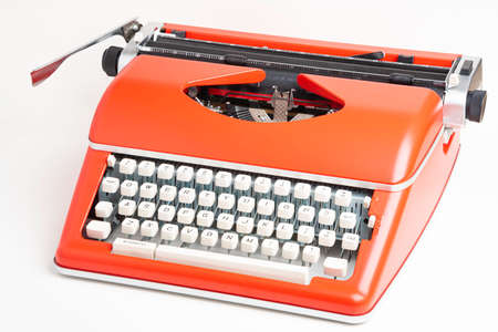 A studio shot of a retro-style portable manual typewriter with ivory-color plastic keyboard and red-orange metal casing.の写真素材