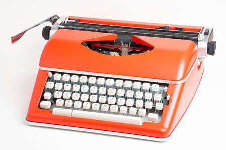 A studio shot of a retro-style portable manual typewriter with ivory-color plastic keyboard and red-orange metal casing.の写真素材