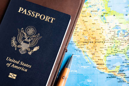 The foil-stamped dark blue front cover of an American passport with leather-covered travel notebooks and writing pen set on a world map background.の写真素材