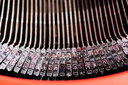 A close-up or macro shot of the type bars of a retro style manual typewriter encased in a hinged red...