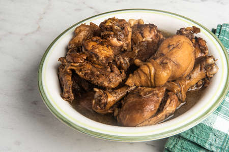 A serving of Filipino-style chicken adobo dish in a bowl with green napkin set on a marble tabletop.の写真素材