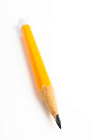 A close-up or macro shot with selective focus of a sharpened classic yellow-orange hexagonal pencil stub set on plain white paper.の写真素材