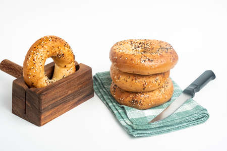 A single tall stack of three freshly baked bagels on a napkin with one bagel on a cutting wood stand and knife set on a plain white background.の写真素材